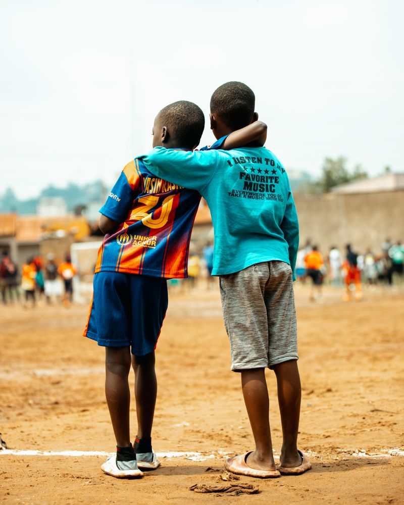 Two young boys standing together with an arm around each other on a football field in Kampala, Uganda